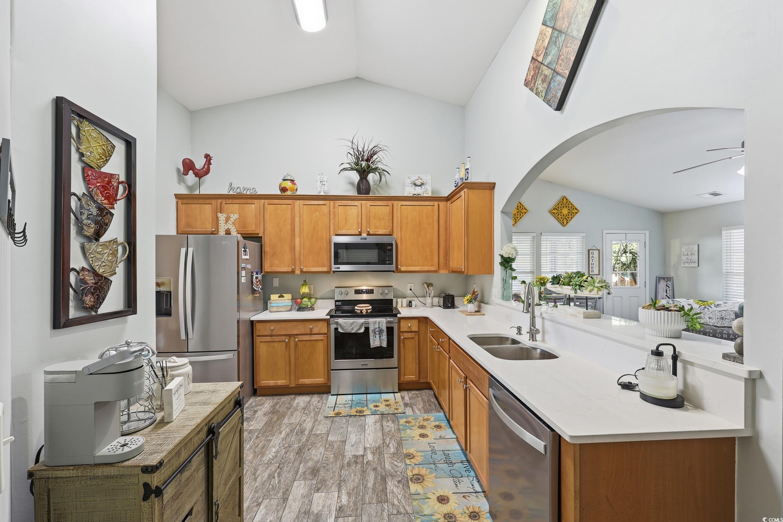 236 Devonbrook Place Longs, SC 29568 - Photo 12 of 40 Kitchen featuring appliances with stainless steel finishes, arched walkways, brown cabinets, light wood-style floors, and light stone countertops
