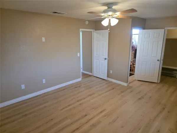 a view of an empty room with wooden floor and a ceiling fan