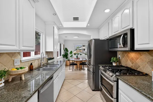 a kitchen with stainless steel appliances granite countertop a stove top oven a sink dishwasher a dining table and chairs with wooden floor