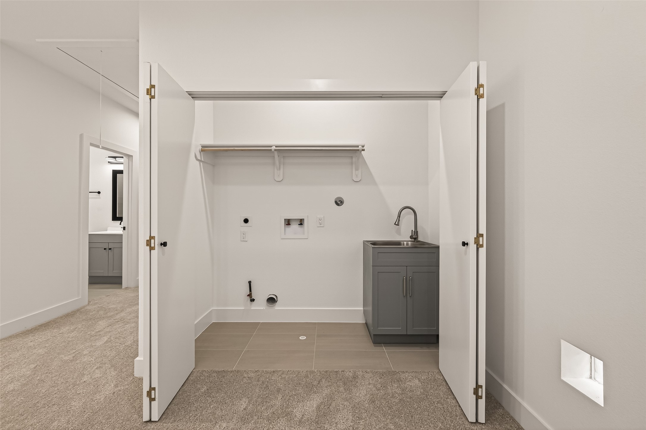 6808 Madrid Street Houston, TX 77021 - Photo 16 of 31 This photo shows a laundry area with open double doors revealing hookups for a washer and dryer, a small sink with a cabinet, and a shelf for storage. The room has carpeted flooring leading to a tiled section.