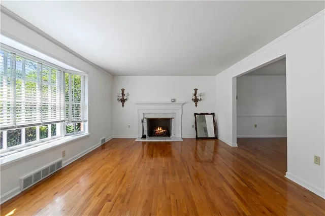 a view of an empty room with wooden floor fireplace and a window