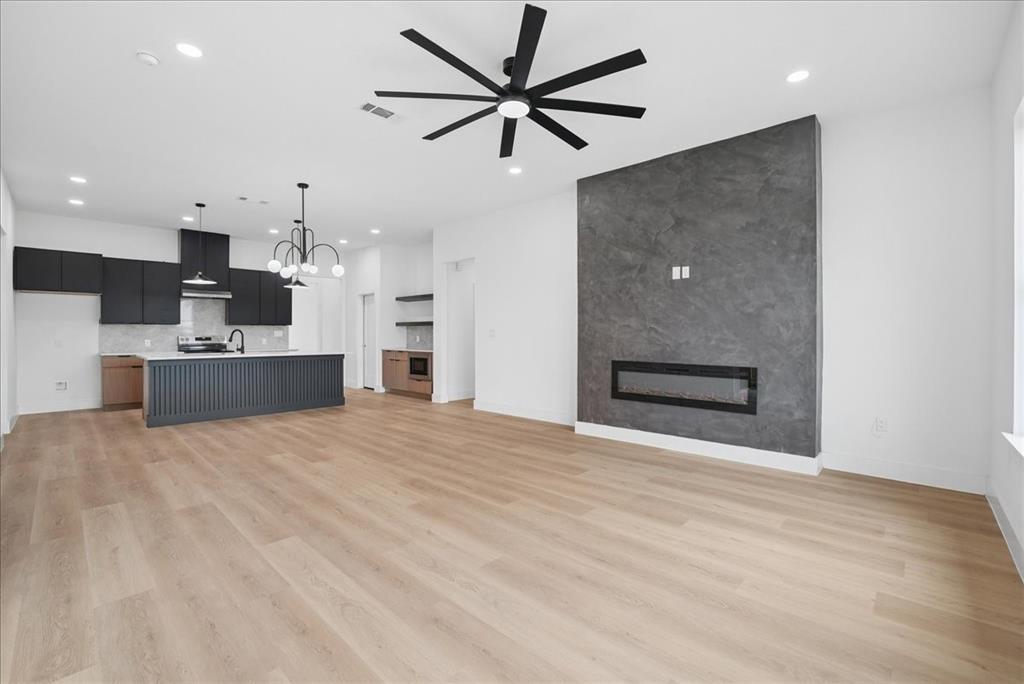 1648 West Wintergreen Road Lancaster, TX 75134 - Photo 14 of 23 Open-concept living area with wood-finish flooring, a modern linear fireplace, and a sleek kitchen featuring dark cabinetry and a central island with a decorative slatted facade