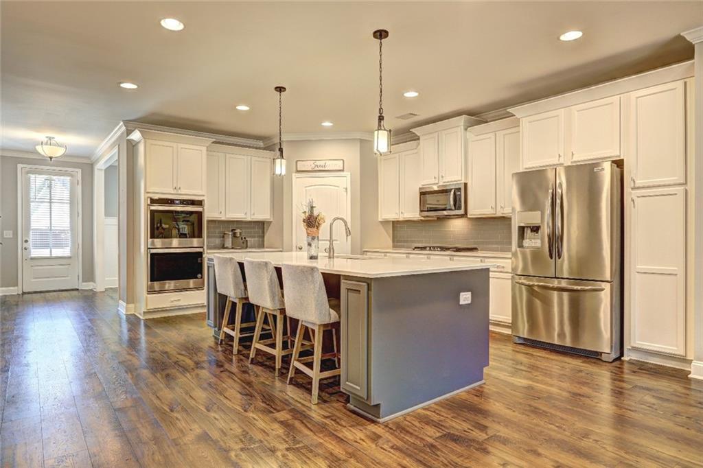 4371 Thacker Lane Suwanee, GA 30024 - Photo 4 of 52 a kitchen with stainless steel appliances granite countertop a refrigerator a stove a sink a dining table and chairs with wooden floor