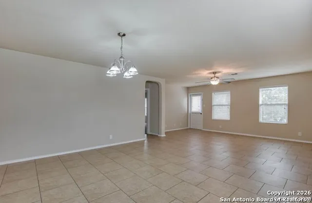 an empty room with chandelier fan and windows