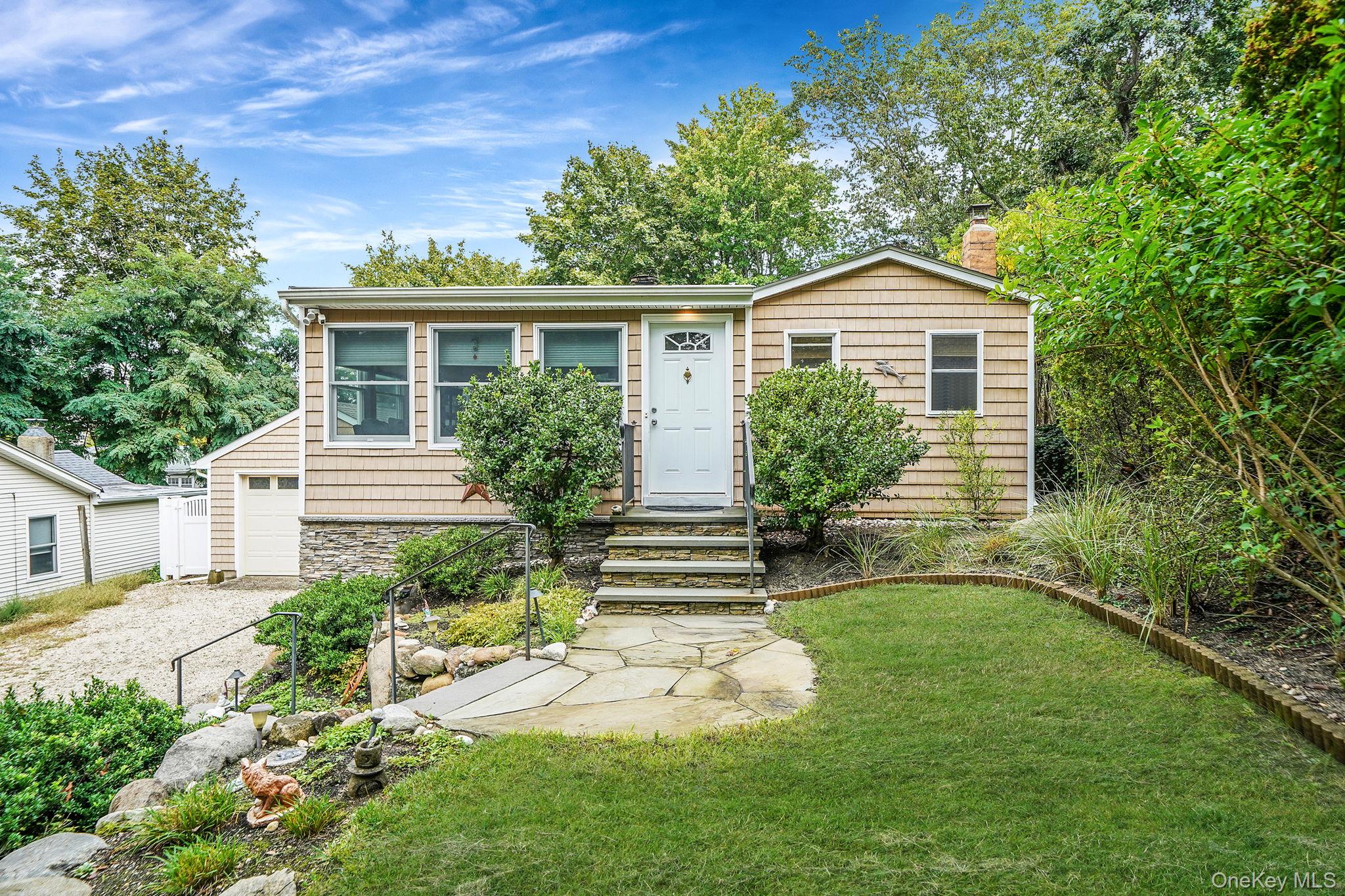 View of front facade featuring a garage, a front lawn, a chimney, stone siding, and driveway
