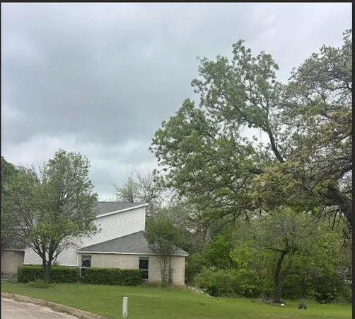 a view of a white house next to a yard with big trees