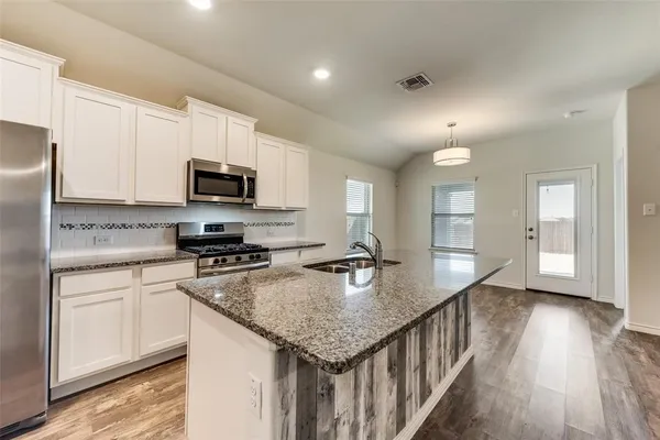 a kitchen with stainless steel appliances granite countertop a sink dishwasher a stove and a refrigerator with wooden floor