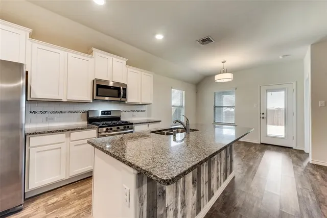 a kitchen with stainless steel appliances granite countertop a sink dishwasher a stove and a refrigerator with wooden floor