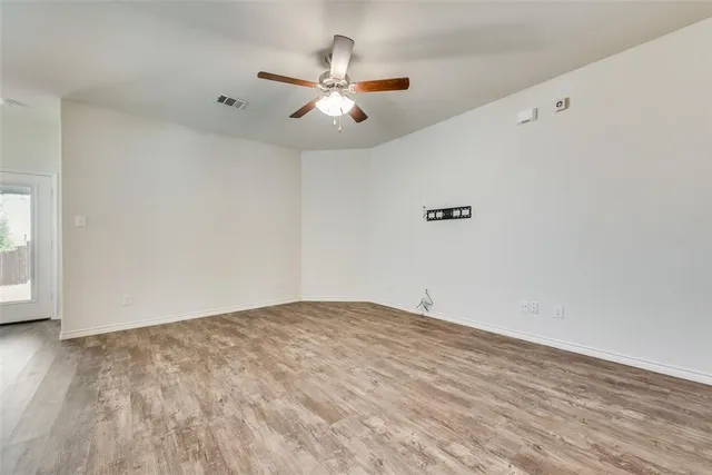an empty room with wooden floor fan and windows