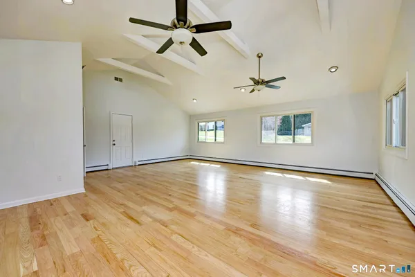 an empty room with wooden floor ceiling fan and windows