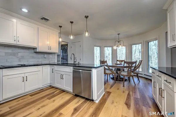 a kitchen with stainless steel appliances granite countertop wooden floor a dining table chairs and white cabinets