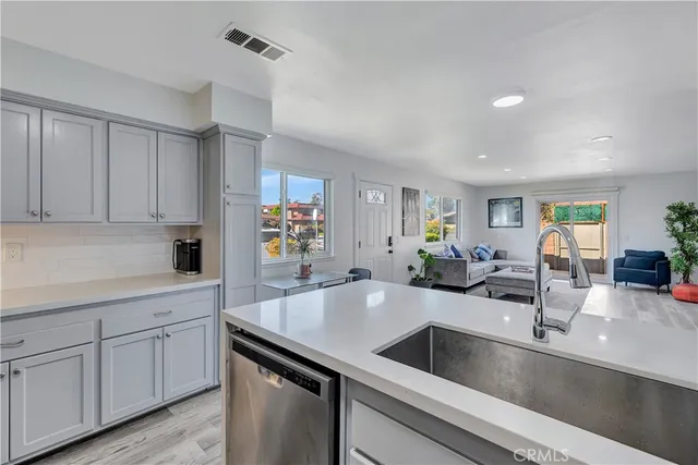 a kitchen with a sink dishwasher and white cabinets with wooden floor