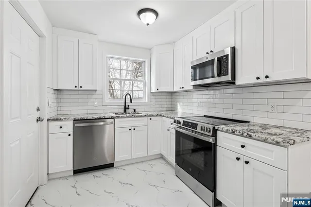 a kitchen with stainless steel appliances granite countertop white cabinets a sink a stove a microwave and island