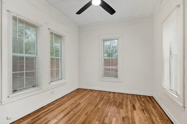 an empty room with wooden floor fan and windows