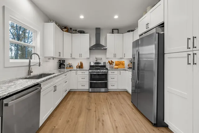 a kitchen with stainless steel appliances granite countertop a refrigerator a sink dishwasher a stove and white countertops with wooden floor