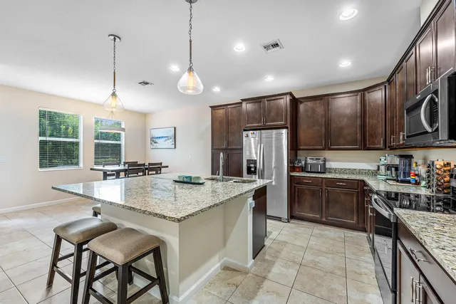 a kitchen with stainless steel appliances granite countertop a sink a stove a refrigerator and a dining table with wooden cabinets