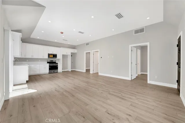 a view of empty room with wooden floor and kitchen