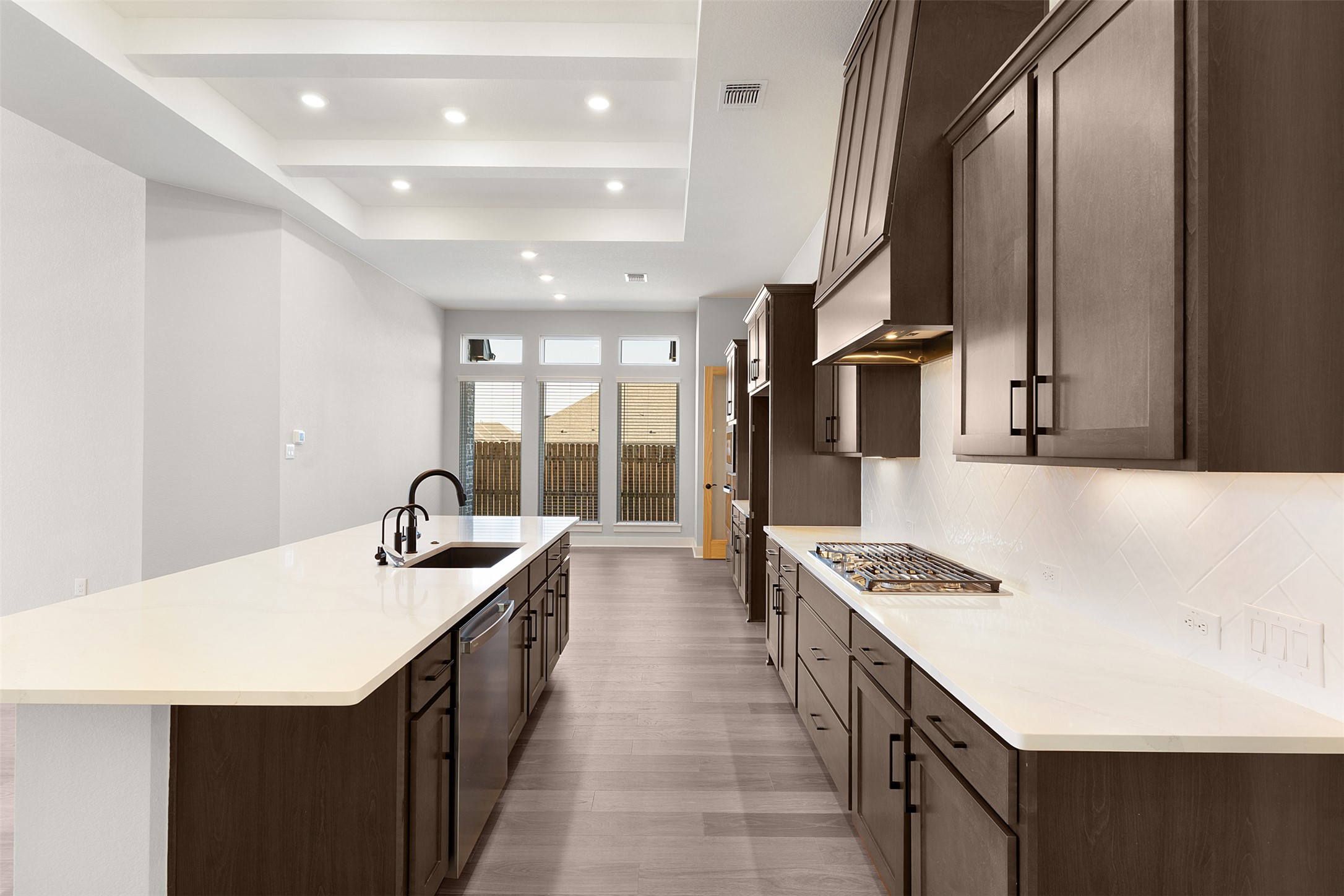 17216 Hope Bergman Road Pflugerville, TX 78660 - Photo 7 of 30 Kitchen with dark brown cabinets, a large island with sink, recessed lighting, backsplash, and a tray ceiling