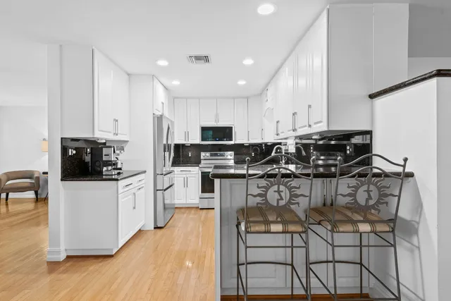 a kitchen with stainless steel appliances kitchen island granite countertop a stove a sink a refrigerator and white cabinets with wooden floor