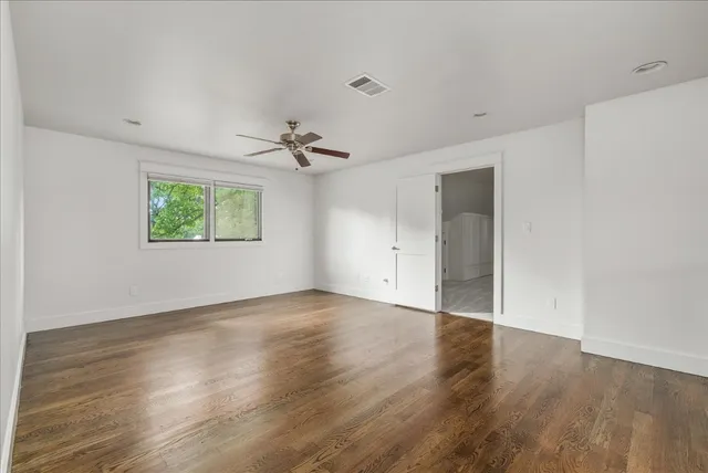 an empty room with wooden floor chandelier fan and windows