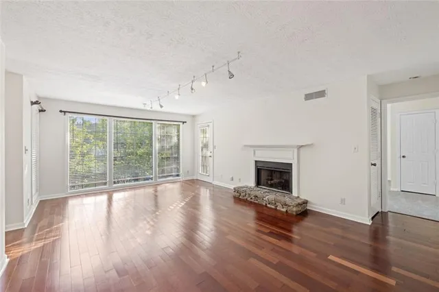 a view of an empty room with wooden floor fireplace and a window