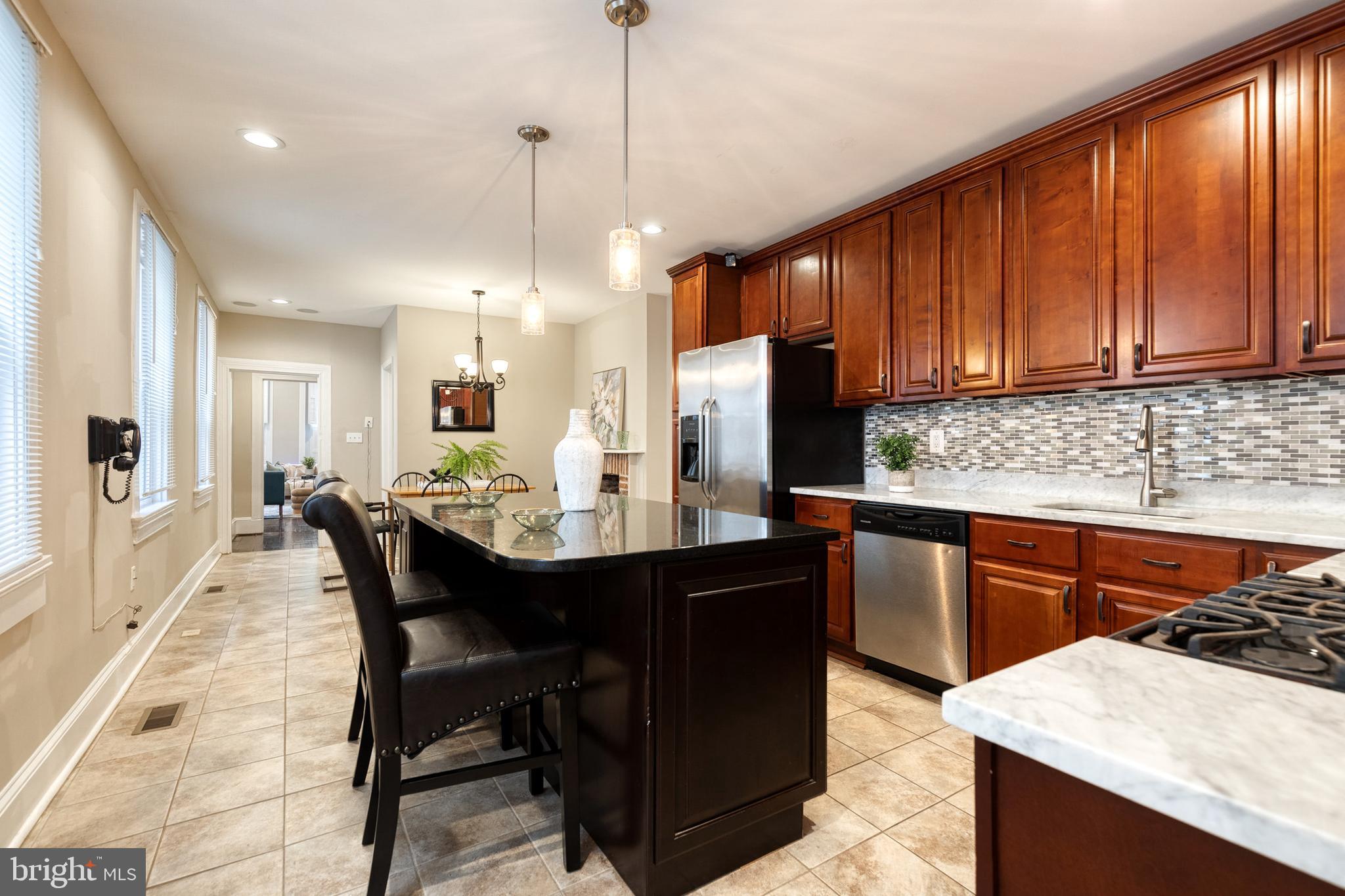 a kitchen with stainless steel appliances granite countertop wooden cabinets a refrigerator a sink a stove a dining table and chairs with wooden floor
