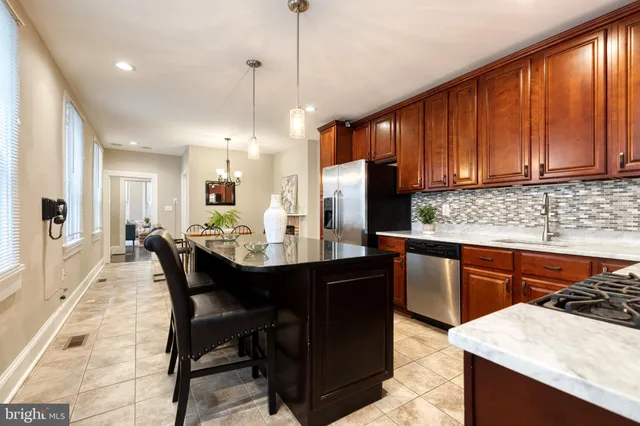 a kitchen with stainless steel appliances granite countertop wooden cabinets a refrigerator a sink a stove a dining table and chairs with wooden floor