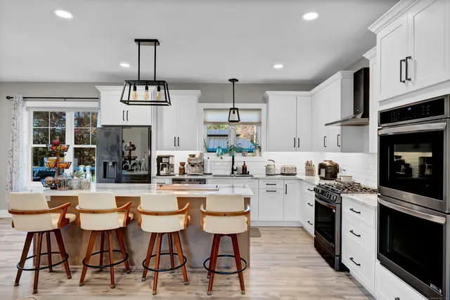 a kitchen view with stainless steel appliances kitchen island granite countertop a refrigerator oven a sink a dining table and chairs with wooden floor