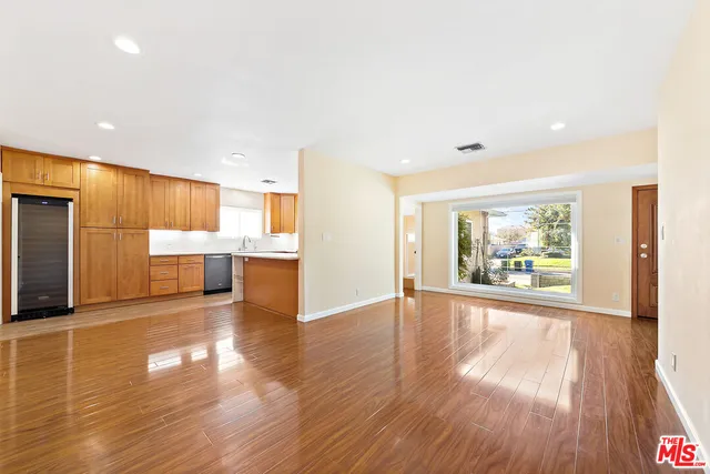 a view of an empty room with wooden floor and a kitchen