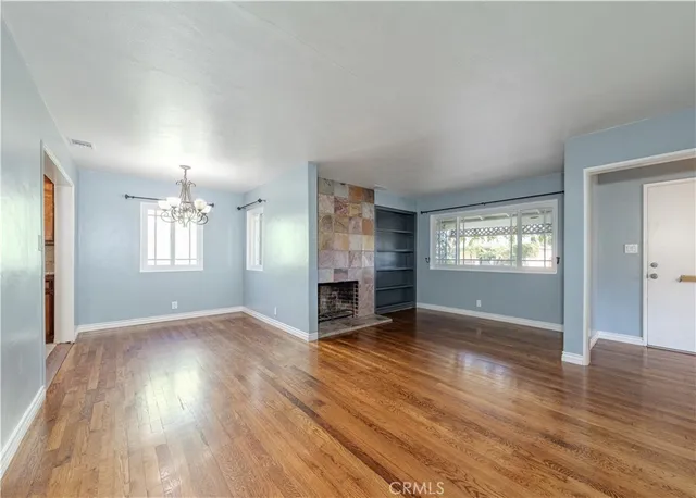 an empty room with wooden floor fireplace and windows