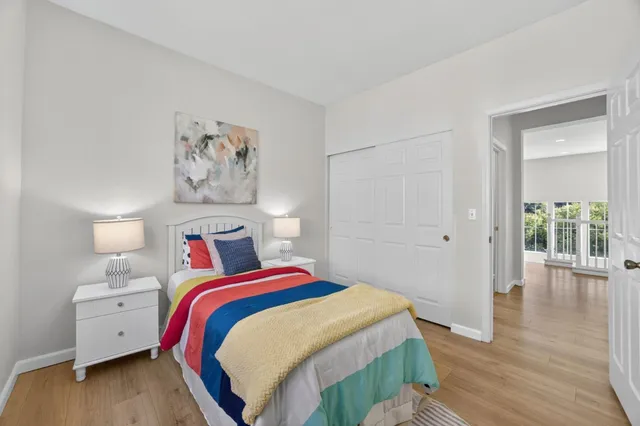 a bedroom with a bed and a lamp on dresser with wooden floor