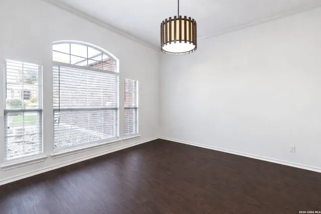 an empty room with wooden floor chandelier and windows