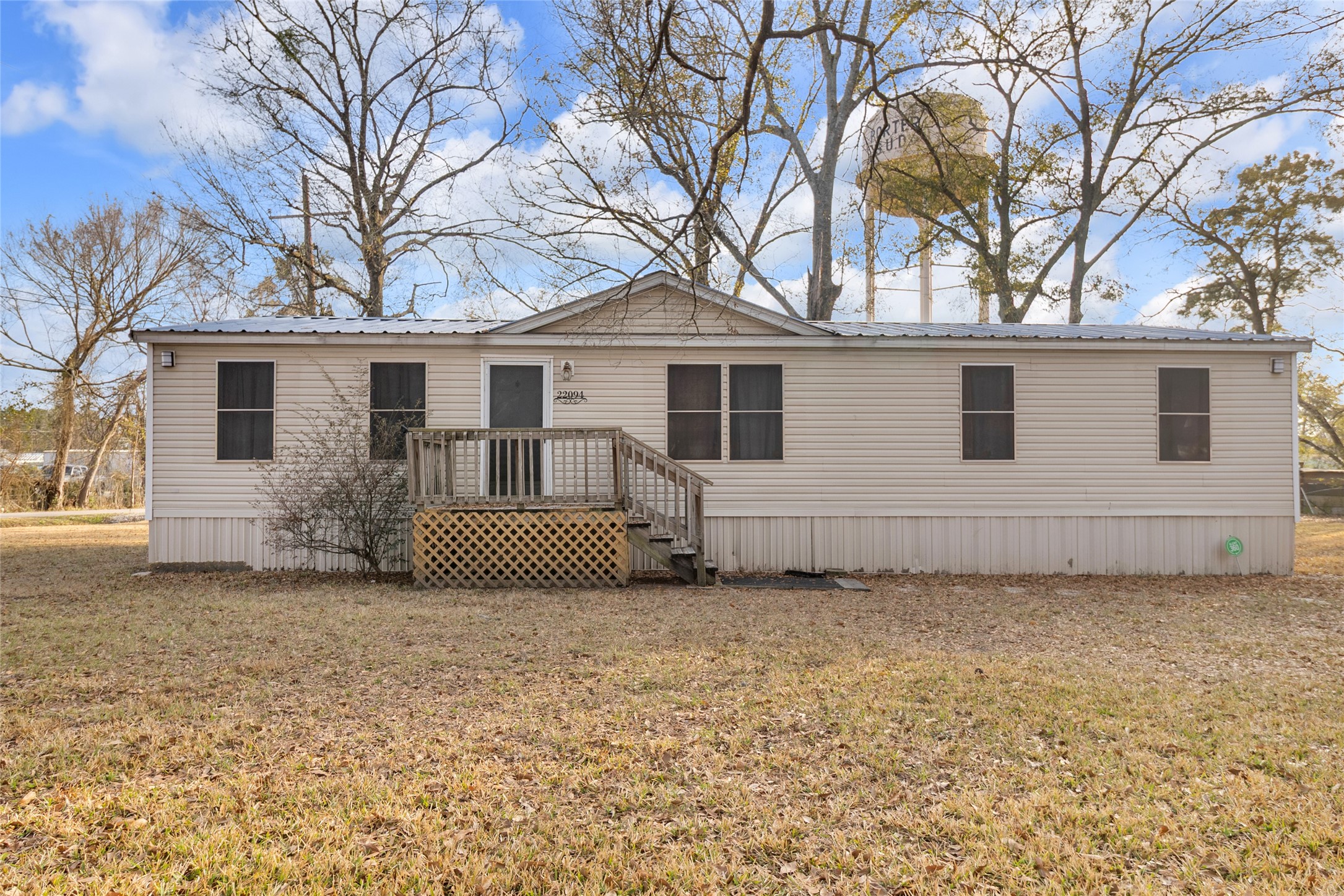22094 Spear Road Porter, TX 77365 - Photo 1 of 45 Single story manufactured home with a small wooden porch and steps leading to the entrance. It's set on a spacious grassy lot with some trees, offering a simple and quiet rural atmosphere.