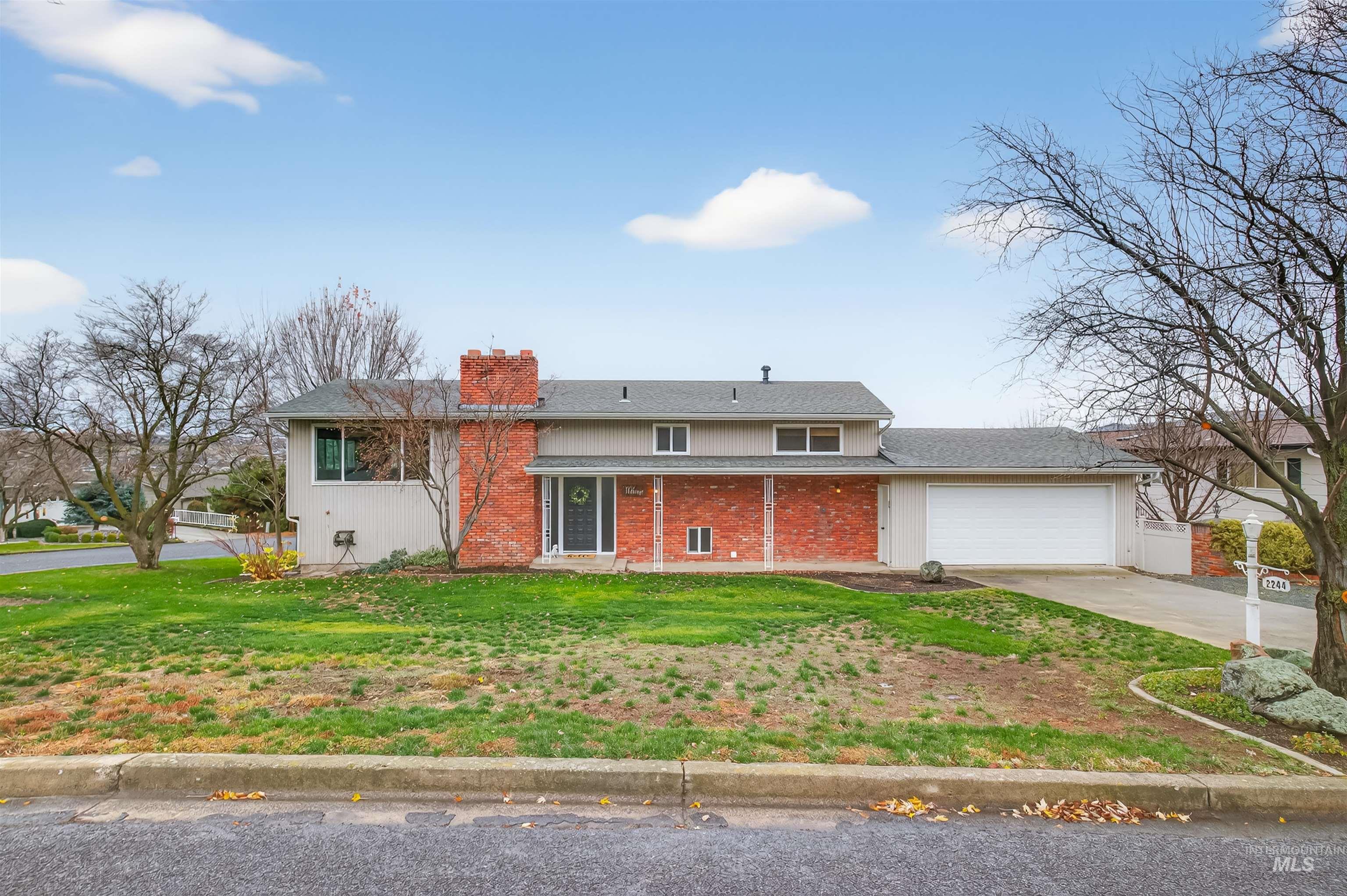 View of front of property featuring a front lawn, brick siding, a chimney, driveway, and a porch