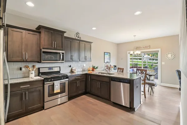 a kitchen with stainless steel appliances granite countertop a stove top oven a sink dishwasher a dining table and chairs with wooden floor