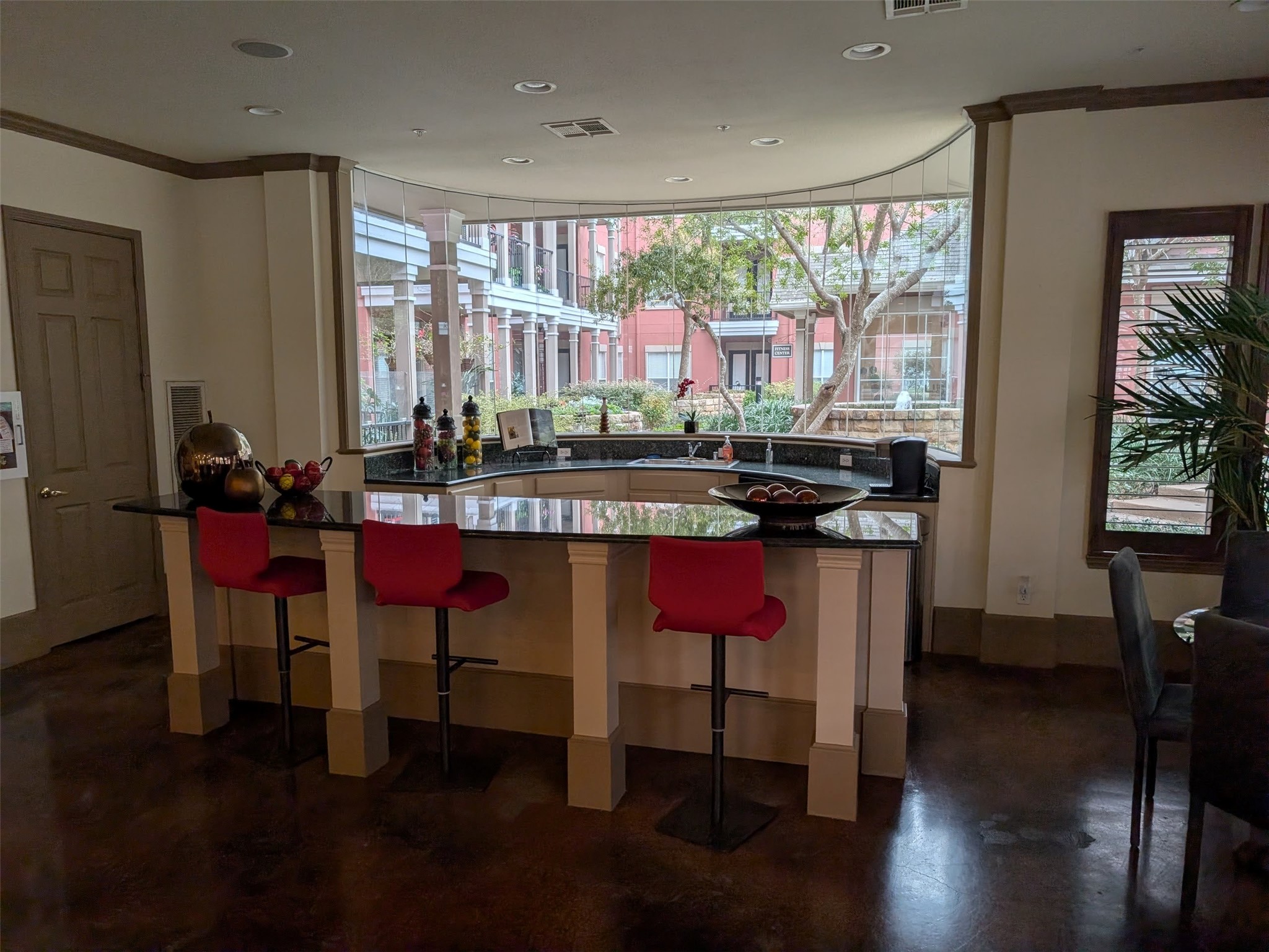 2400 McCue Road, Unit 136 Houston, TX 77056 - Photo 22 of 25 This photo showcases a modern kitchen area with a sleek black countertop, three red barstools, and large windows offering a view of a courtyard. The space is well-lit and features elegant décor, creating a warm and inviting atmosphere.
