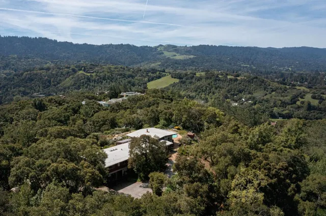 an aerial view of a house with swimming pool and large trees