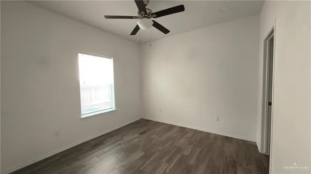 an empty room with wooden floor ceiling fan and windows