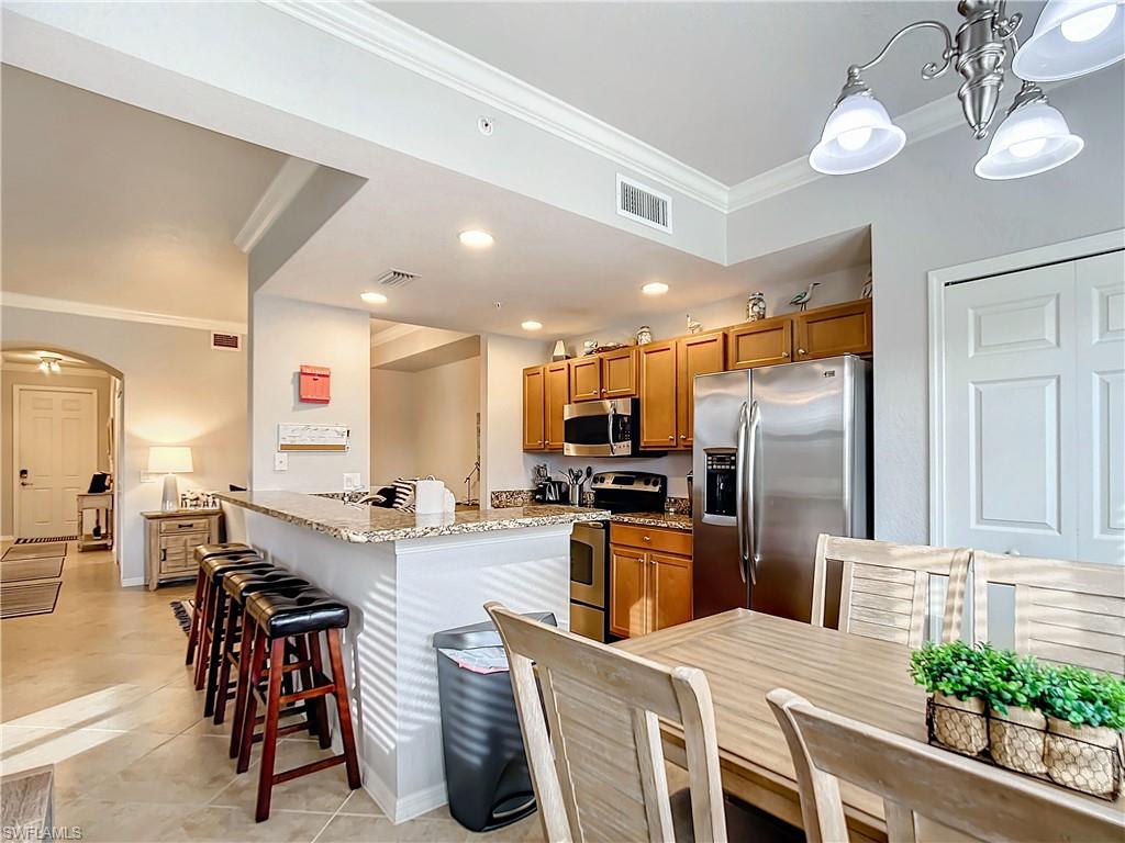 9715 Acqua Court, Unit 127 Naples, FL 34113 - Photo 22 of 50 a kitchen with stainless steel appliances kitchen island granite countertop a refrigerator a stove a sink a dining table and chairs with wooden floor