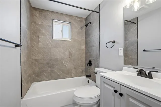 a bathroom with a granite countertop bathtub shower sink vanity mirror and toilet