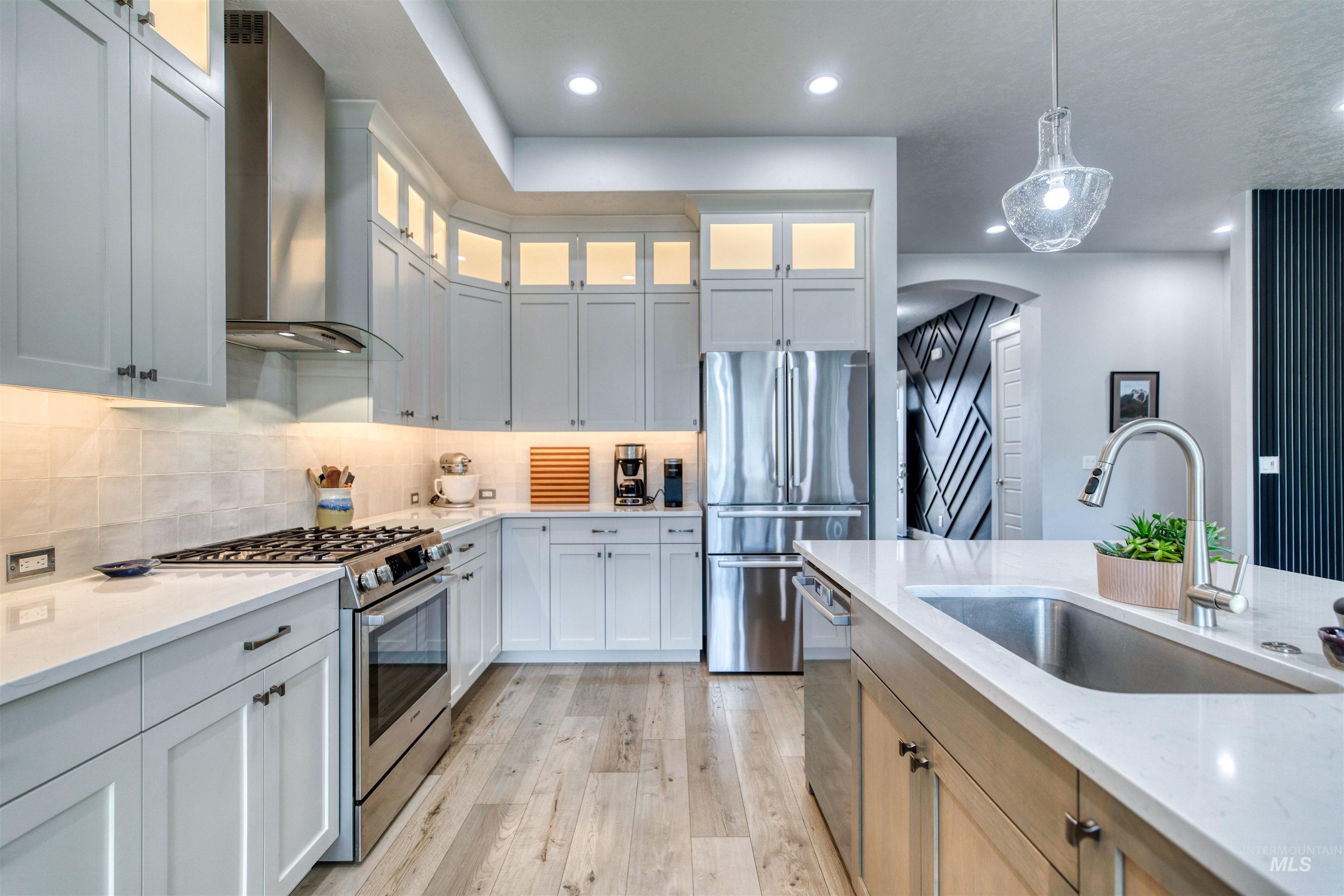 795 East Rio Chico Drive Kuna, ID 83634 - Photo 9 of 34 Kitchen featuring stainless steel appliances, decorative light fixtures, wall chimney range hood, light stone countertops, and glass insert cabinets