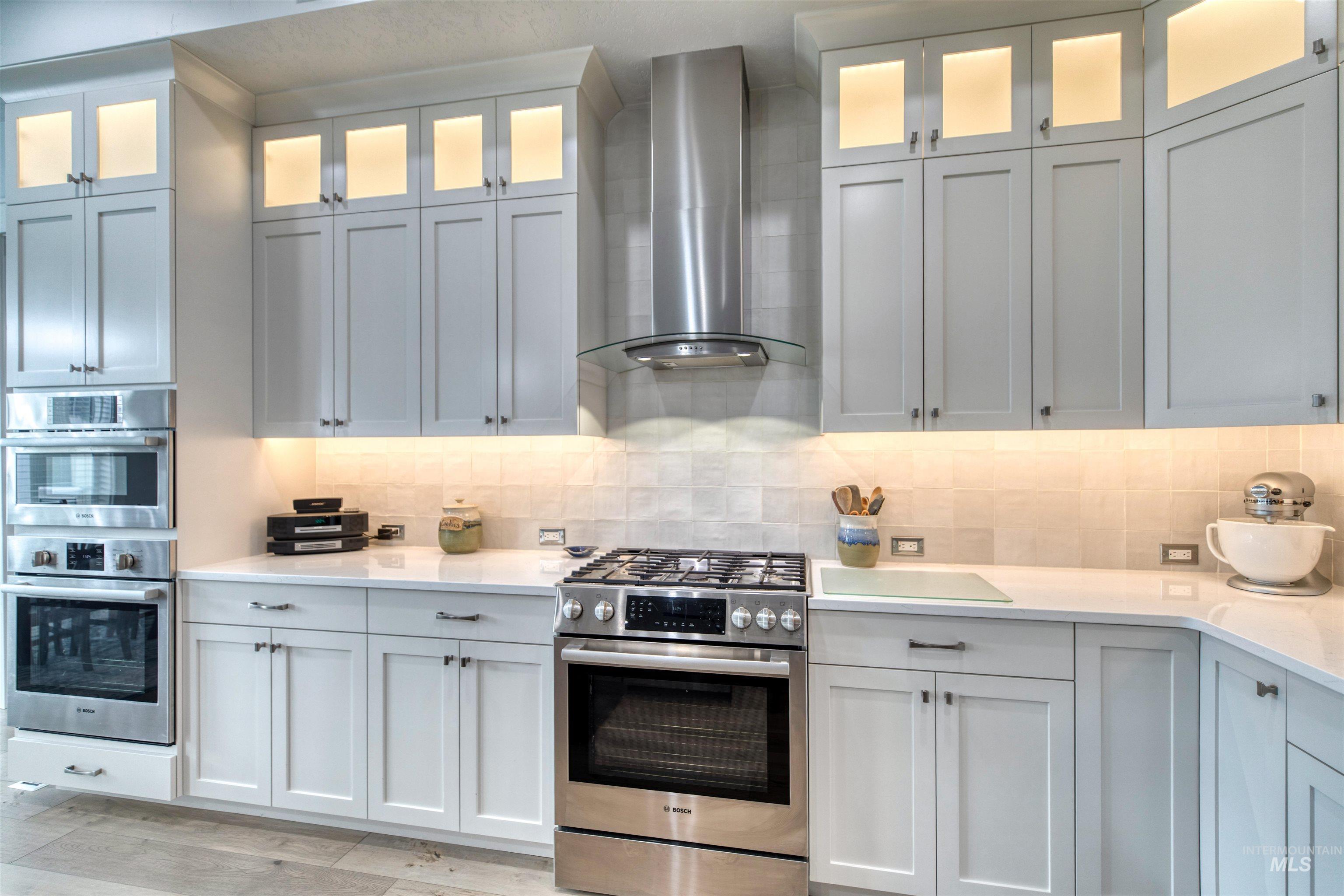 795 East Rio Chico Drive Kuna, ID 83634 - Photo 10 of 34 Kitchen with appliances with stainless steel finishes, wall chimney exhaust hood, light stone counters, decorative backsplash, and white cabinets