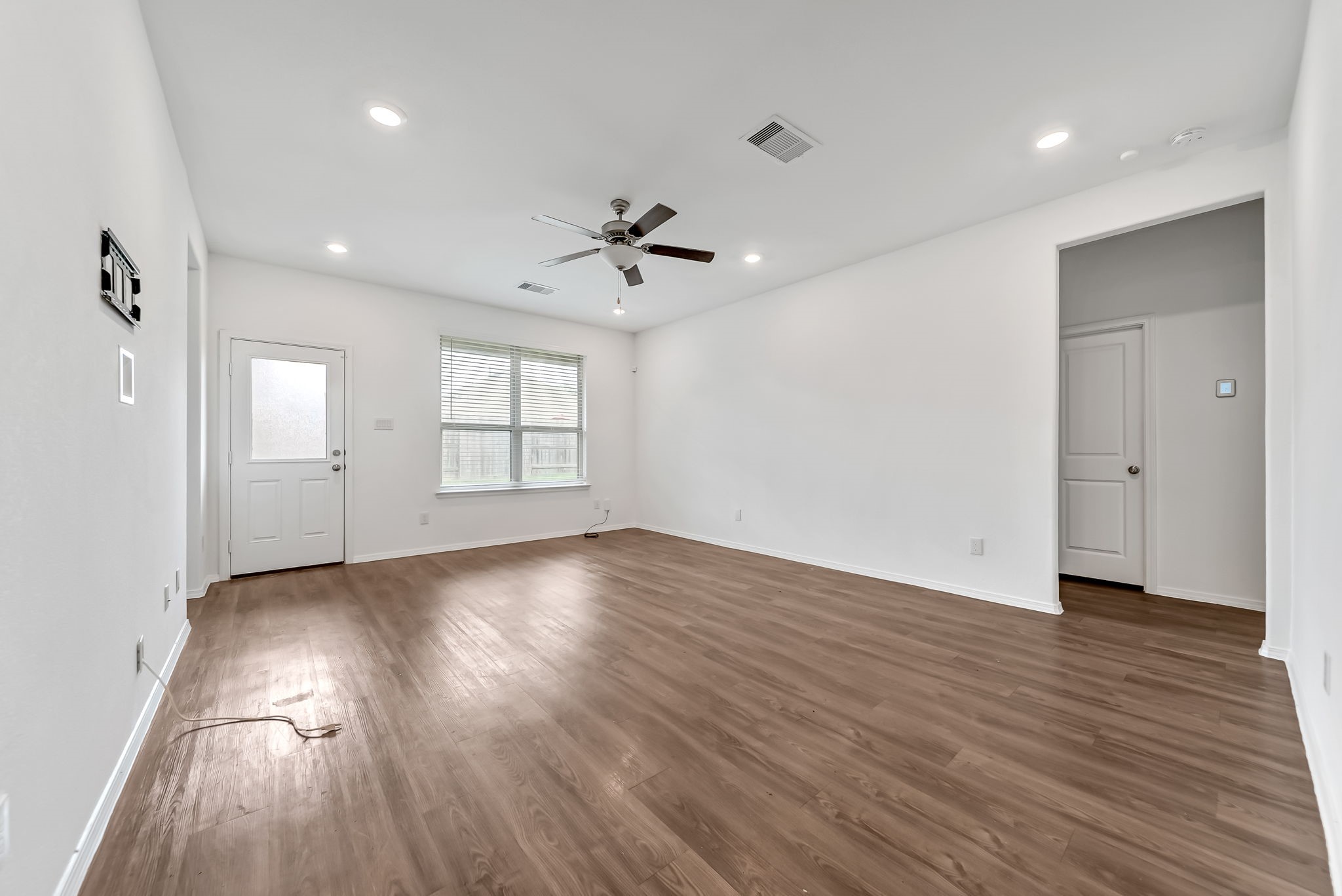 2847 Mistygate Court Conroe, TX 77301 - Photo 2 of 27 Spacious living room with wood flooring, neutral walls, and recessed lighting. Features a ceiling fan, large window for natural light, and a door leading outside. Ideal for versatile living arrangements.