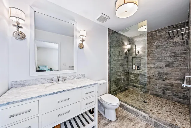 a bathroom with a granite countertop sink a toilet a mirror and shower