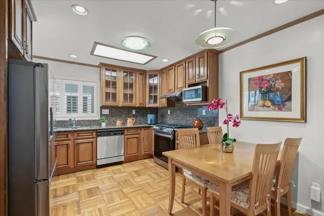 a kitchen with stainless steel appliances granite countertop a stove top oven a sink a dining table and chairs with wooden floor