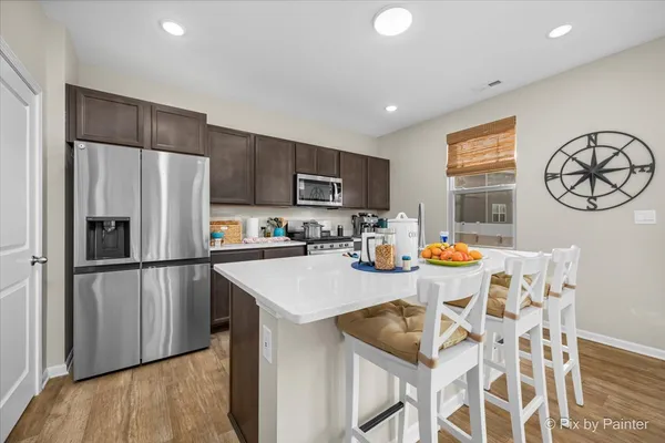 a kitchen with stainless steel appliances granite countertop a refrigerator a sink a stove a dining table and chairs with wooden floor