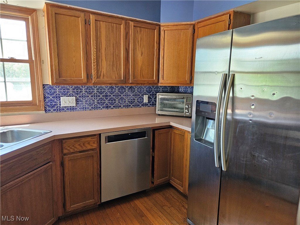 6247 Hathaway Road Cleveland, OH 44125 - Photo 14 of 42 Kitchen with appliances with stainless steel finishes, light countertops, dark wood-style floors, brown cabinets, and decorative backsplash