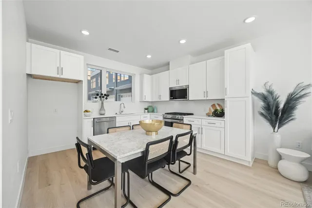 a kitchen with stainless steel appliances granite countertop a stove top oven a sink a refrigerator and white cabinets with wooden floor