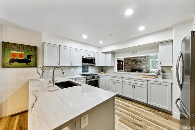 a kitchen with stainless steel appliances kitchen island granite countertop a refrigerator a stove a sink dishwasher and white cabinets with wooden floor