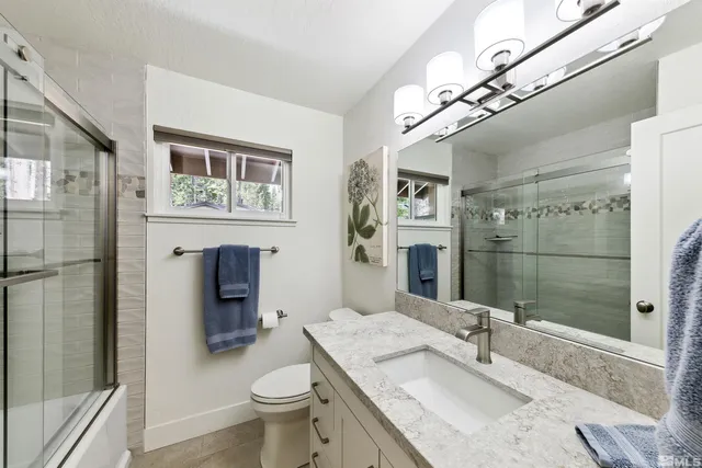 a bathroom with a granite countertop sink a toilet a large mirror and shower
